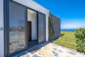 Ein modernes Gebäude mit großen Glasüren, einem pflasterbelagten Eingangsbereich und Blick aufs Meer.