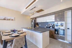 A modern kitchen with a central island, stainless steel appliances, and a dining area with a table set for four. - Villa Nerea - Three Bedroom Villa, Sleeps 6 (Geriş Mahallesi)