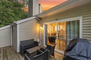 Eine Terrasse mit Gartenmöbeln, einem überdachten Grill und einer Glastür zu einem Innenbereich.