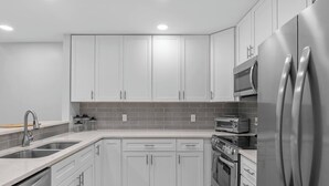 A modern kitchen with white cabinets, stainless steel appliances, and a tiled backsplash. - Coastal Gem near Wrightsville Beach, Golf & Dining (Wilmington)