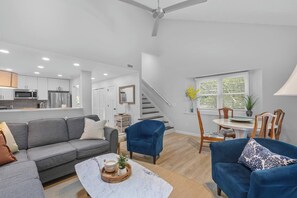 Un salon moderne avec un canapé gris, des fauteuils bleus, une table basse en marbre et un coin repas comprenant une table et des chaises.