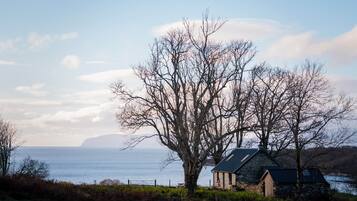 Un paysage côtier avec un bâtiment en pierre, un grand arbre sans feuilles et une vue sur la mer.