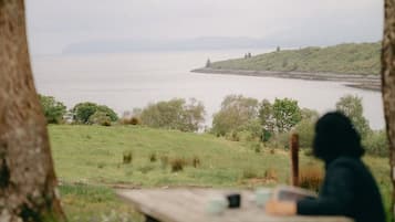 Une table de pique-nique avec une personne assise, d’où l’on peut admirer un plan d’eau et un paysage lointain.