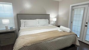 A bedroom with a bed, nightstands, a ceiling fan, and a door. - Central Urban Glam Getaway near Moore, OKC, Norman (Oklahoma City)