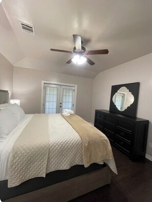 A bedroom with a bed, a ceiling fan, a dresser, and a mirror.
