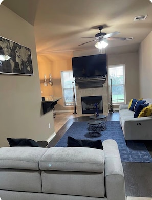 A living room with a fireplace, a ceiling fan, a flat-screen TV, and a sofa.
