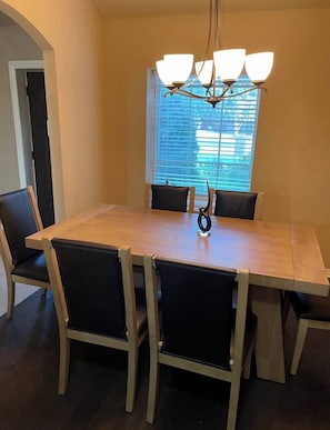 A dining room with a wooden table and black chairs, a chandelier, and a window with blinds.
