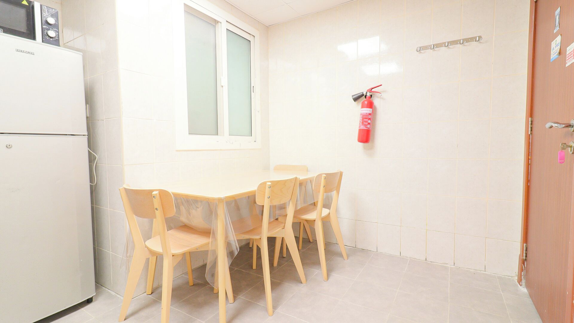 Une petite cuisine équipée d’un réfrigérateur, d’une fenêtre et d’un extincteur fixé au mur.