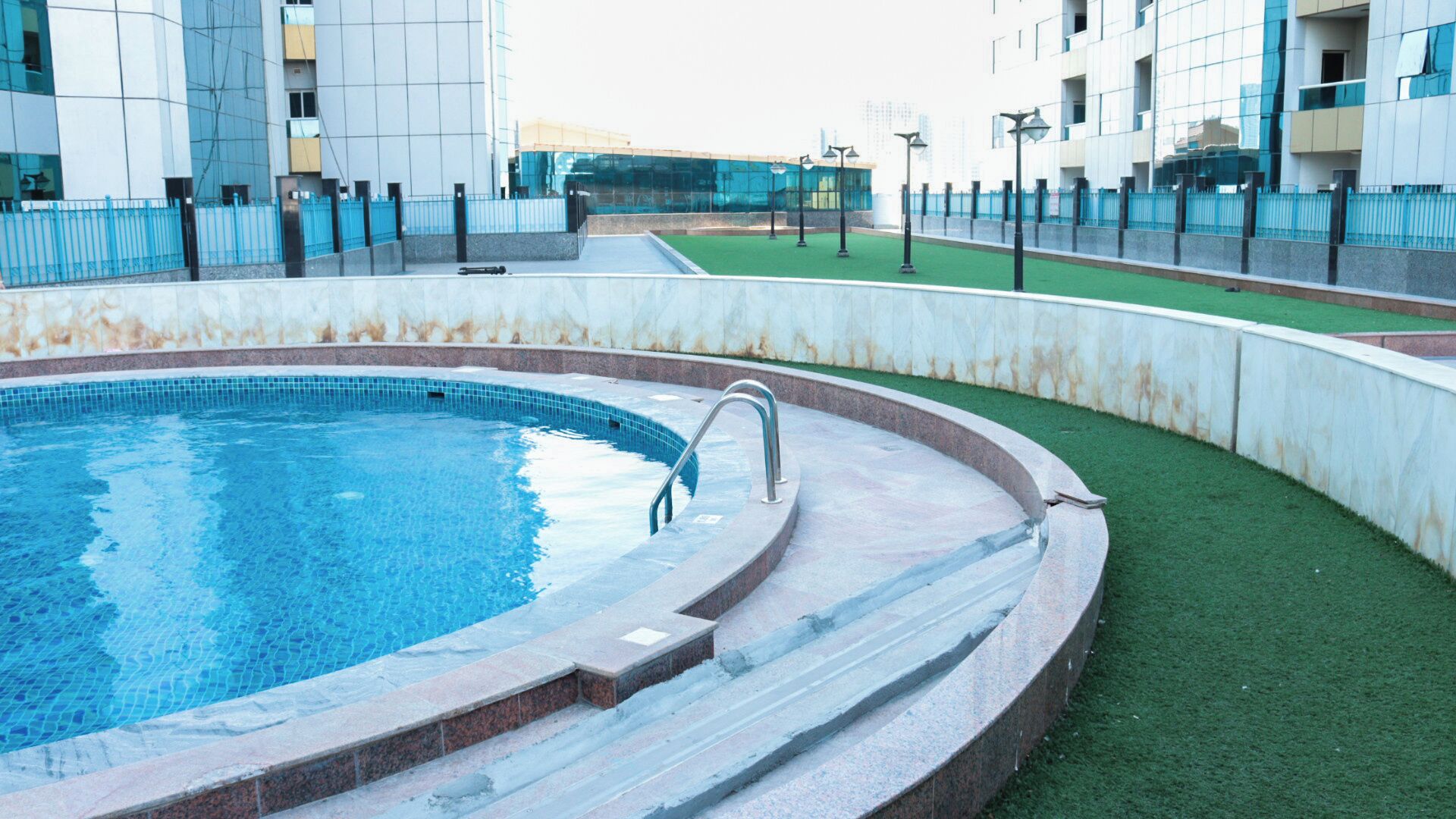 Une piscine à l’eau d’un bleu cristallin, entourée d’une terrasse en pierre et d’une zone recouverte de gazon synthétique vert.