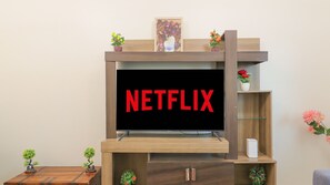 Ein Flachbildfernseher an einer Holz-Unterhaltungseinrichtung, darüber ein Regal mit einem gerahmten Bild und Topfpflanzen.