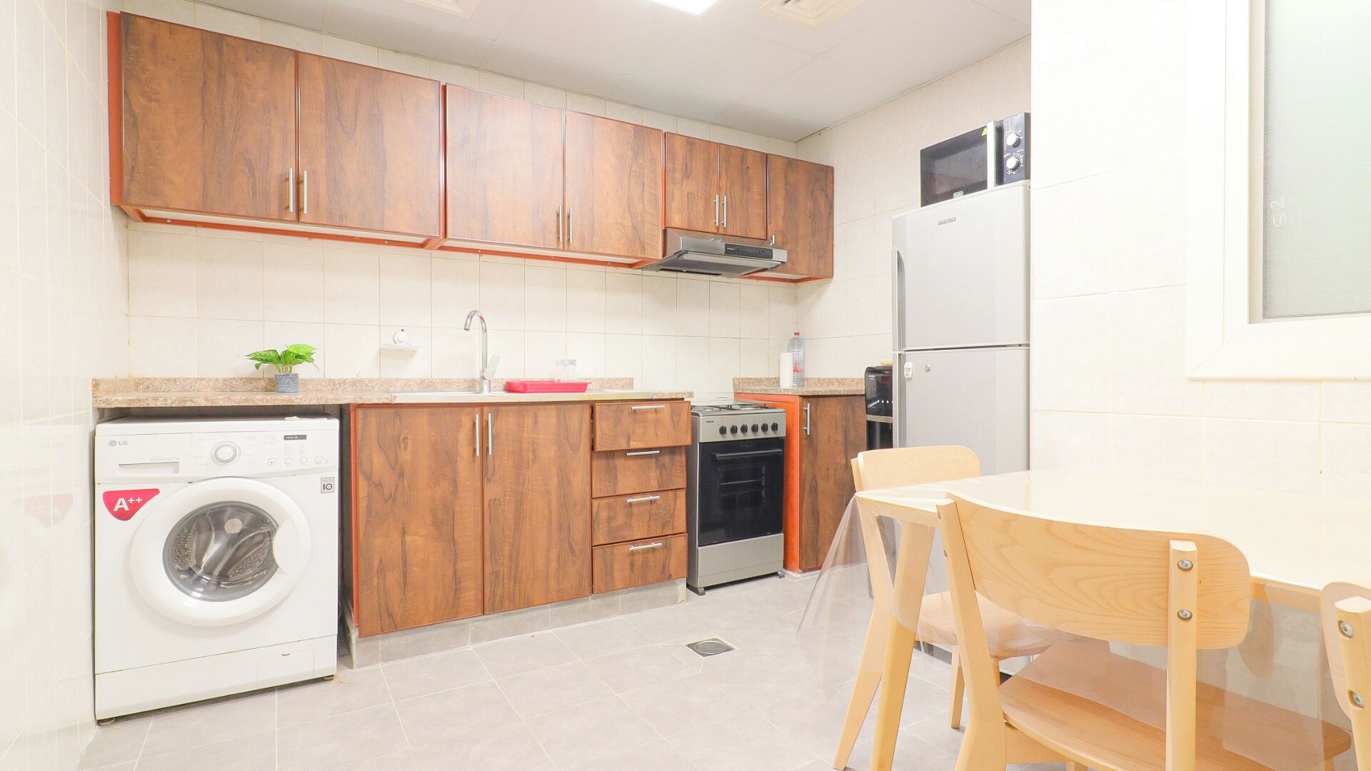 Eine kompakte Küche mit Holzschränken, einer Waschmaschine, einem Backofen und einer Mikrowelle.