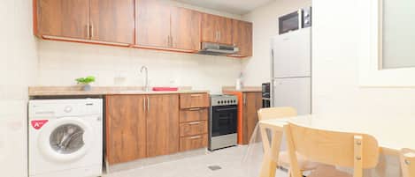 A compact kitchen with wooden cabinets, a washing machine, an oven, and a microwave.