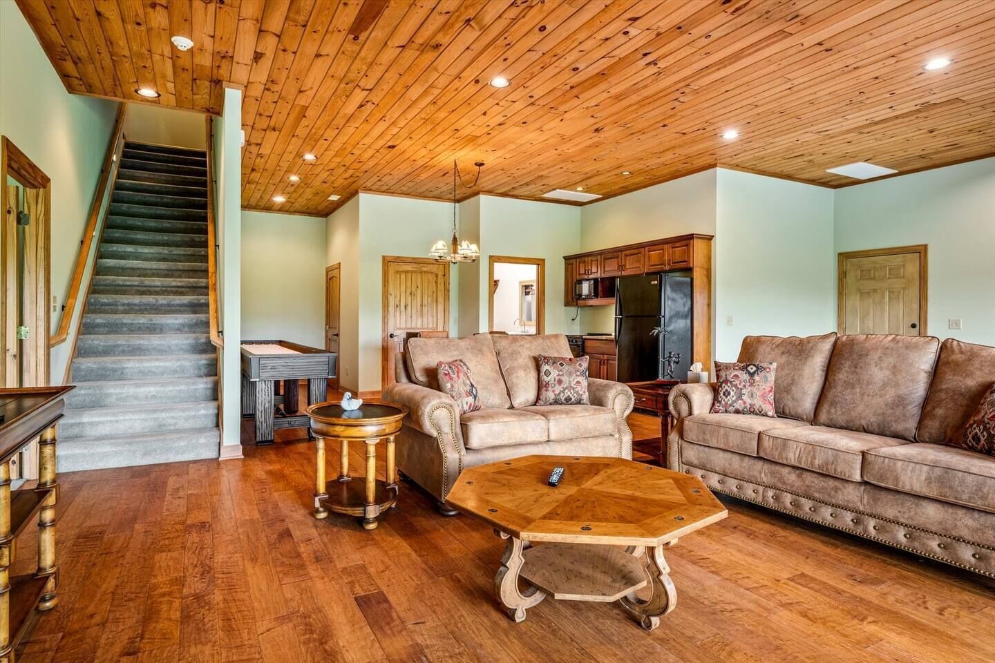 A spacious living room with a wooden staircase, a pool table, a sofa, and a coffee table.