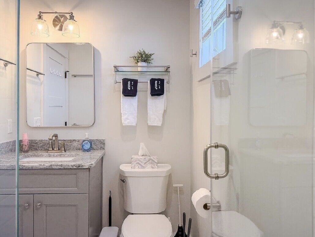 Een badkamer met een glazen douchecabine, een wastafel met een marmeren blad, een toilet en een spiegel met een handdoekhouder erboven.