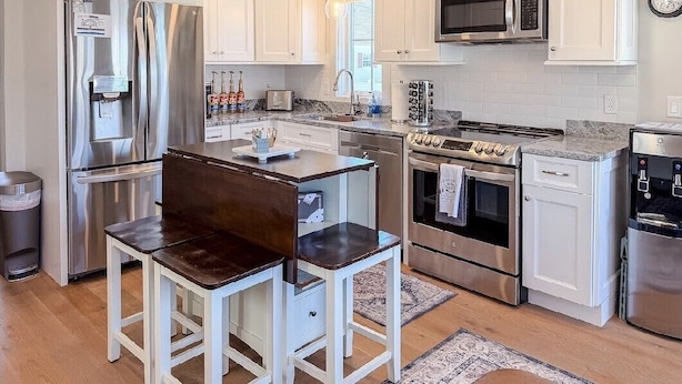 A modern kitchen with white cabinetry, stainless steel appliances, and a central island with seating. - Lakeside 2-bedroom condo in awesome Laconia (Laconia)