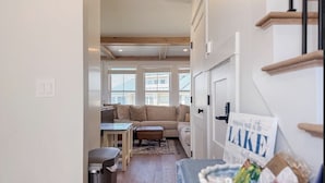 A hallway leading to a living room with a sofa, a small table, and a trash bin. - Lakeside 2-bedroom condo in awesome Laconia (Laconia)