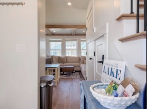 A hallway leading to a living room with a sofa, a small table, and a trash bin. - Lakeside 2-bedroom condo in awesome Laconia (Laconia)