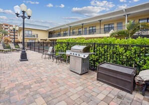 Ein Außenbereich mit Terrasse, Grill, Sitzgelegenheiten und einer Umzäunung.