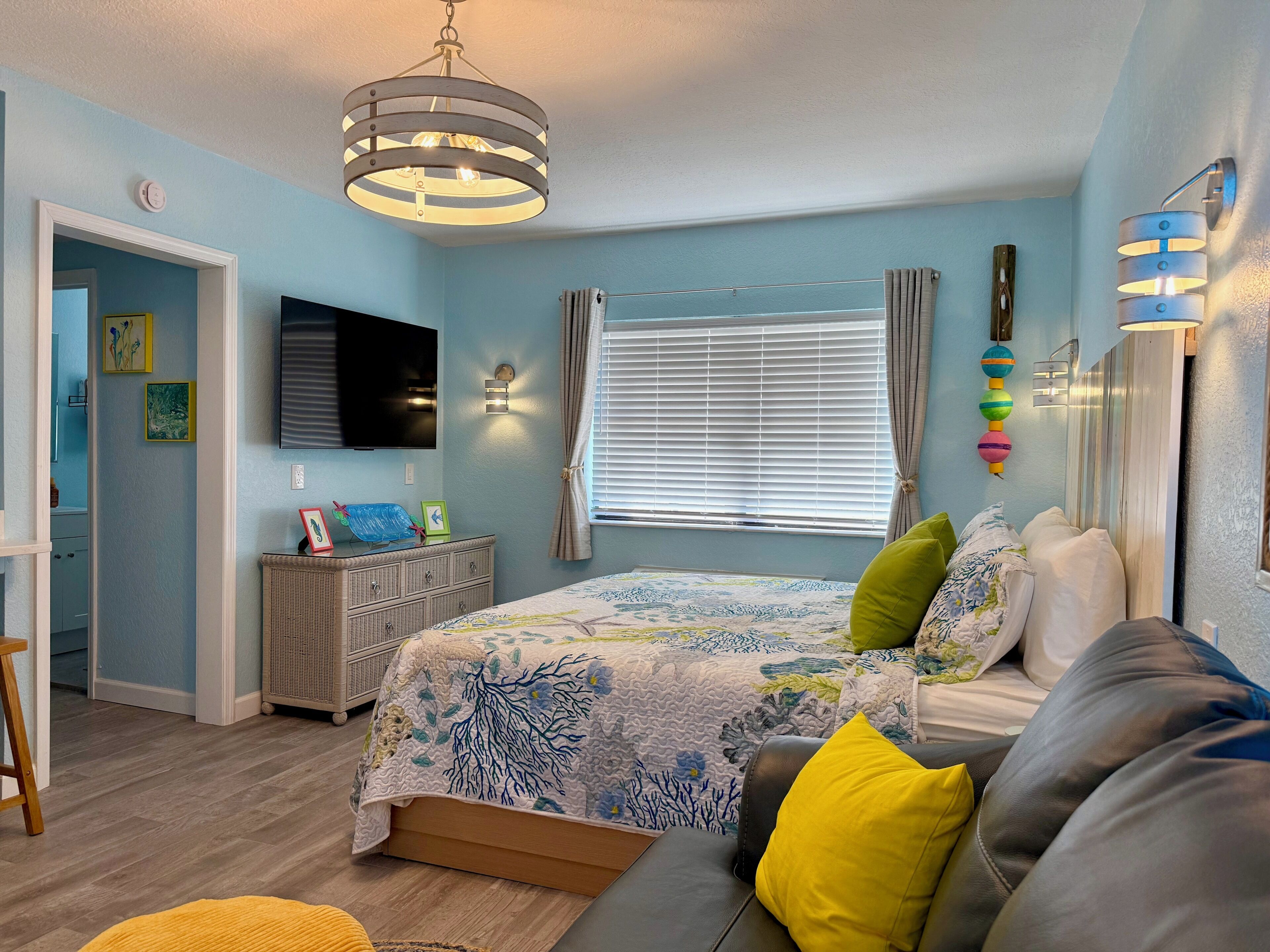 Un dormitorio con cama, sofá, televisor y ventana con cortinas.