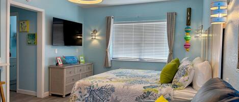 Un dormitorio con cama, sofá, televisor y ventana con cortinas.