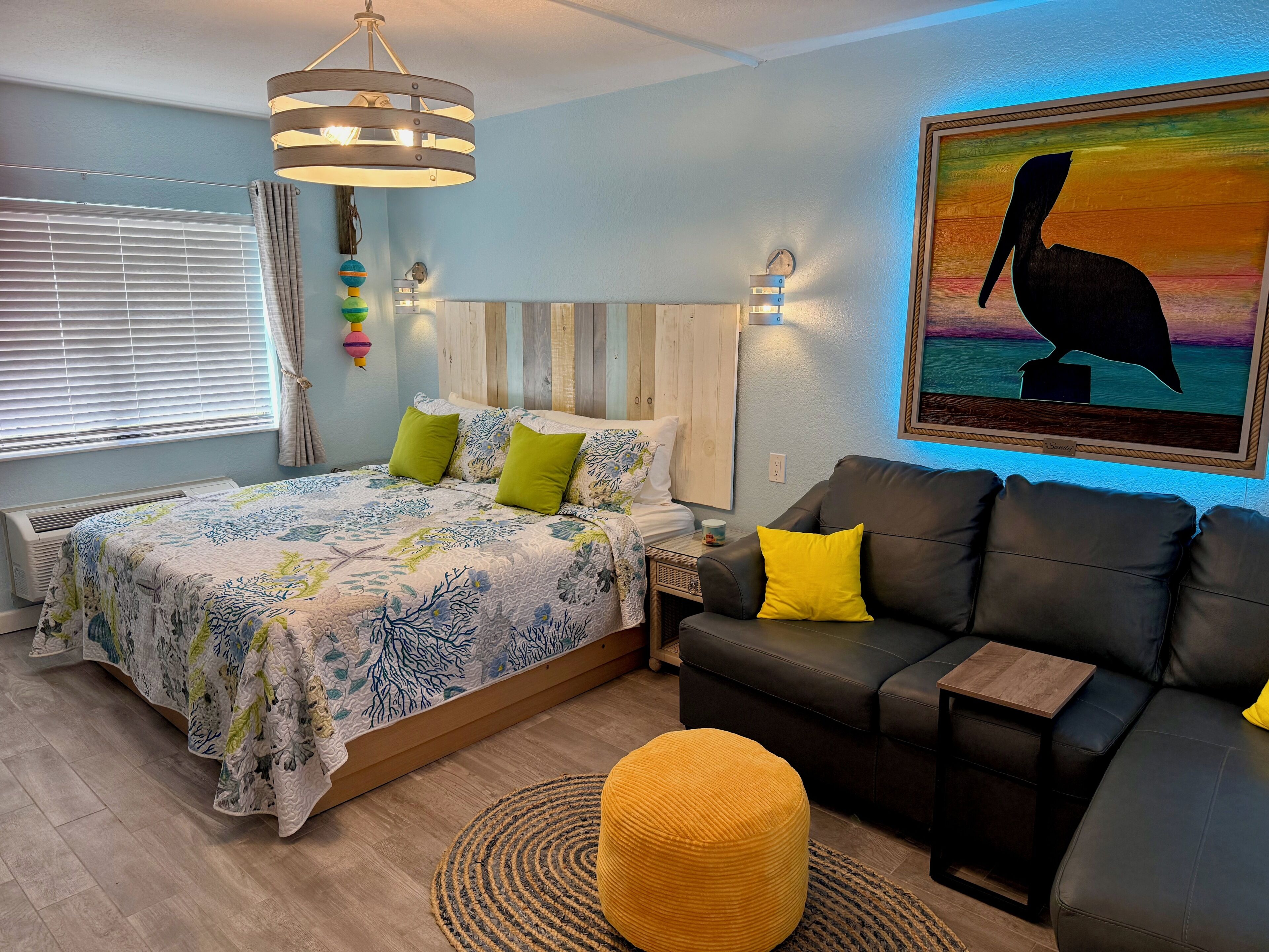 A bedroom with a bed, a sofa, a wall clock, a painting, and a ceiling light fixture.