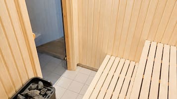 Un sauna avec un banc en bois, un seau et une louche en bois, et un cendrier noir orné de pierres.