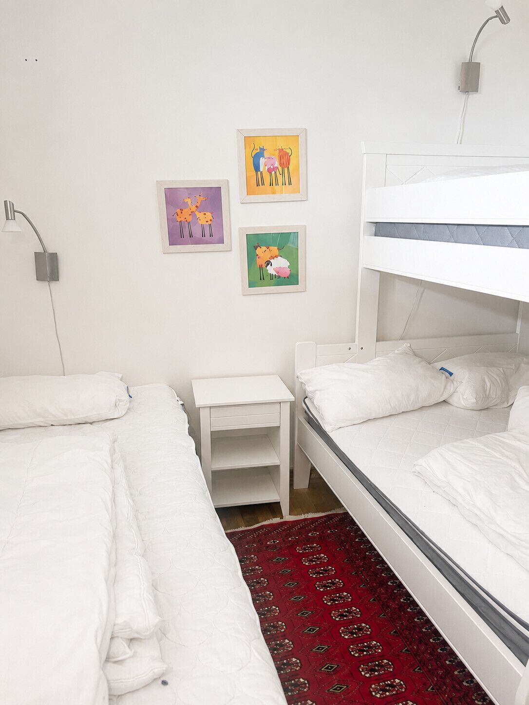 A room with two beds, a bedside table, and a wall-mounted lamp.