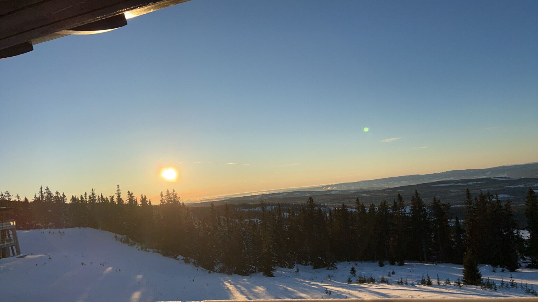 Een besneeuwd landschap met een heldere lucht en een lage zon aan de horizon, wat duidt op zonsopkomst of zonsondergang.