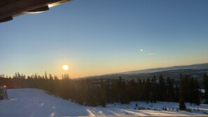 Eine verschneite Landschaft mit blauem Himmel und tiefstehender Sonne, was entweder Sonnenaufgang oder Sonnenuntergang andeutet.