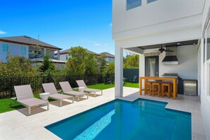 A modern outdoor pool area with lounge chairs and a barbecue setup. - New Luxury 30A Beach Home plus Pool and more. (Santa Rosa Beach)