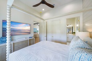 A bedroom with a large bed, a television, a ceiling fan, and a view of the outdoors.