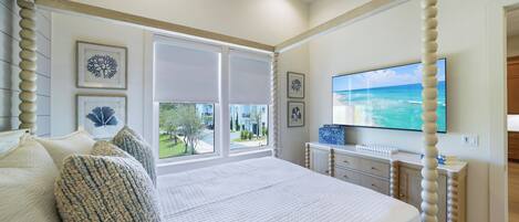 Un dormitorio con una cama grande, un televisor montado en la pared y vistas al exterior por la ventana.