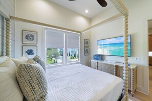 A bedroom with a large bed, a TV mounted on the wall, and a view of the outdoors through the window. - New Luxury 30A Beach Home plus Pool and more. (Santa Rosa Beach)