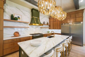 A modern kitchen with marble countertops, a stainless steel refrigerator, and a unique pendant light fixture. - New Luxury 30A Beach Home plus Pool and more. (Santa Rosa Beach)