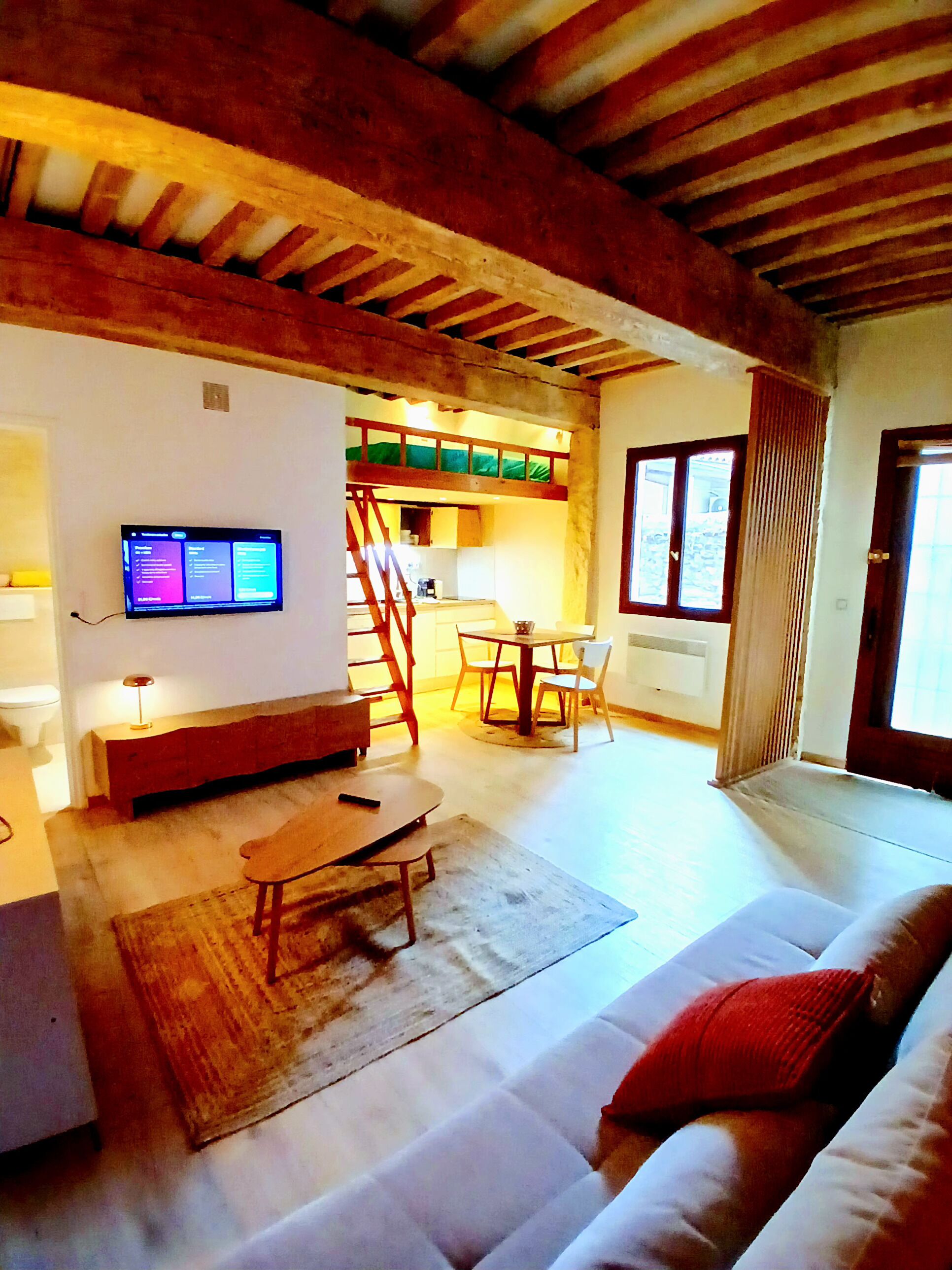 A living room with a sofa, a coffee table, a TV mounted on the wall, and a staircase leading to an upper level.