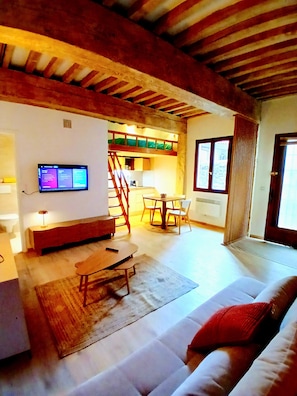 Ein Wohnzimmer mit Sofa, Couchtisch, an der Wand montiertem Fernseher und einer Treppe, die zu einer oberen Ebene führt.