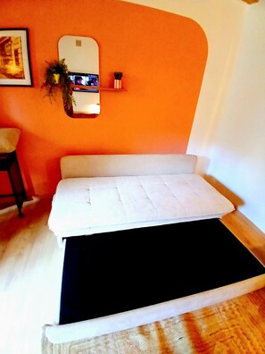 A room with a white sofa against an orange wall, a small table with a plant, and a framed picture on the wall. - Elegant, quiet loft with a mezzanine in the city center; sleeps 1–4 people (Lyon)