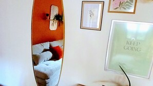 Ein Zimmer mit Spiegel, der ein Bett, ein gerahmtes Bild mit Text und einen Blumentopf auf einem Tisch reflektiert.