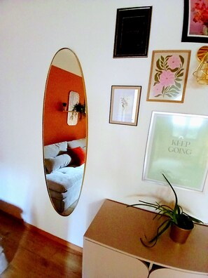 Ein Zimmer mit Spiegel, der ein Bett, ein gerahmtes Bild mit Text und einen Blumentopf auf einem Tisch reflektiert.