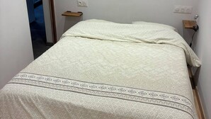 Une chambre à coucher avec un lit, un plancher en bois, une porte donnant sur une autre pièce et une petite table de chevet avec une lampe.