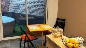 Une cuisine comprenant une table à manger, des chaises, un plan de travail avec un panier de fruits, et une porte-fenêtre coulissante donnant sur un espace patio.