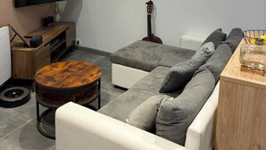Un salon moderne avec un téléviseur à écran plat, une guitare, une table basse ronde en bois et un canapé d’angle.