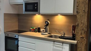 Une cuisine moderne avec des meubles blancs, un four à micro-ondes encastré, une machine à café et une bouteille de vin.