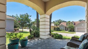 A covered patio area with a stone floor, potted plants, and wicker furniture. - NEW! Beautiful home w/ private pool and golf cart! (Destin)