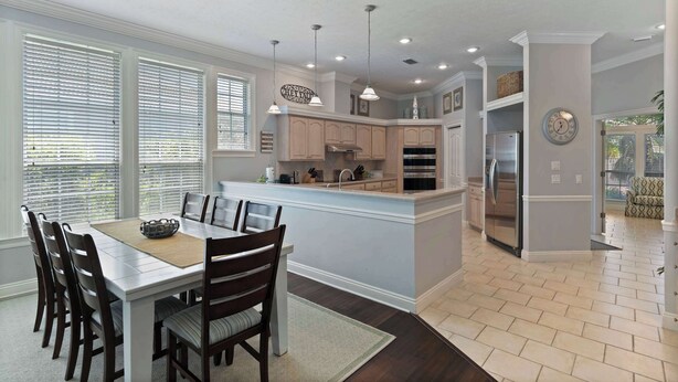 A modern kitchen with a central island, built-in appliances, and a dining area with a table and chairs. - NEW! Beautiful home w/ private pool and golf cart! (Destin)