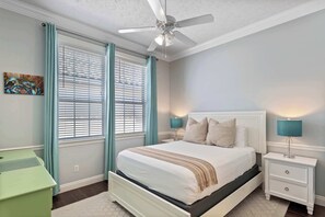 Een slaapkamer met een bed, twee nachtkastjes, een plafondventilator en een raam met jaloezieën.