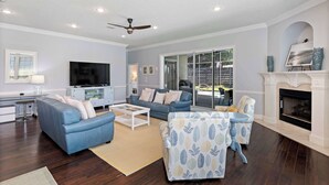 A modern living room with a fireplace, a television, and a seating area with a coffee table. - NEW! Beautiful home w/ private pool and golf cart! (Destin)