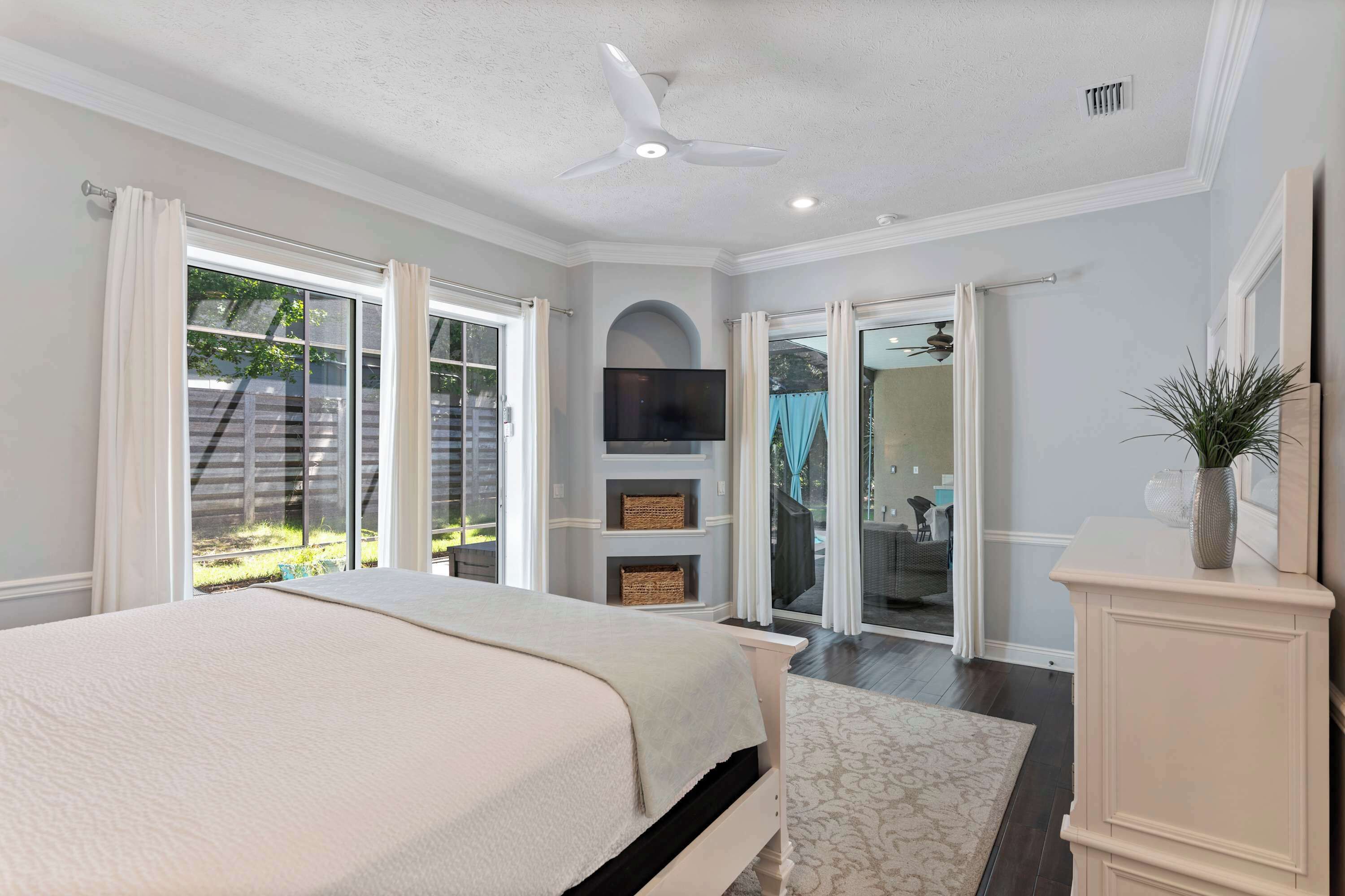 A bedroom with a bed, a ceiling fan, a TV, and a sliding glass door leading to a patio.