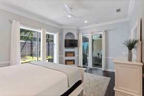 Ein Schlafzimmer mit einem Bett, einem Deckenventilator, einem Fernseher und einer Glastür, die zu einer Terrasse führt.