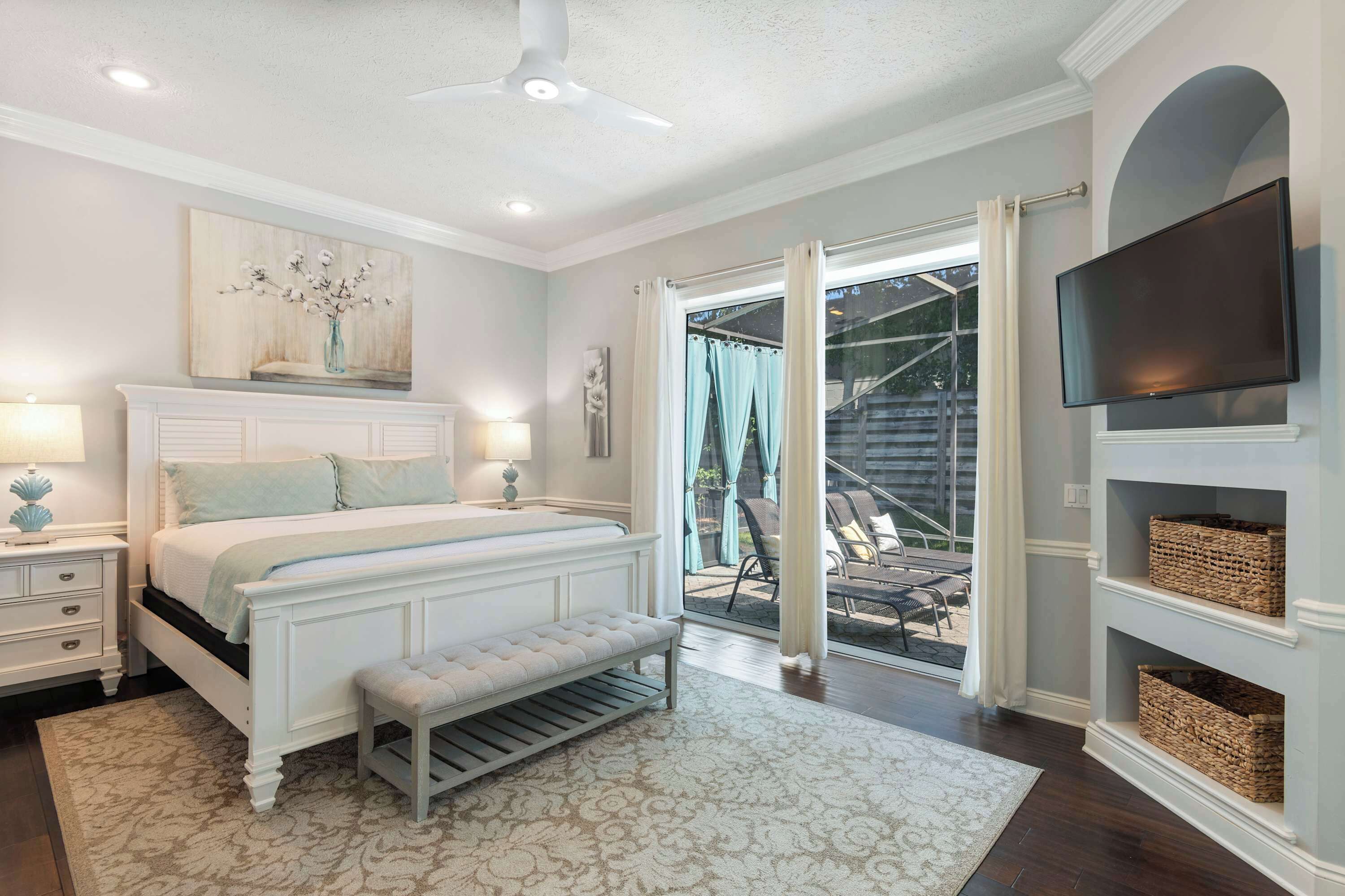A bedroom with a bed, bedside tables, a bench, a TV, and a view of the outdoors.